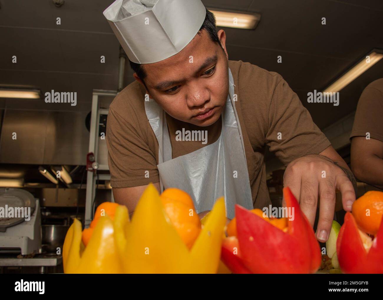 220317-N-DM318-1010 INSTALLATION AÉRIENNE NAVALE ATSUGI, Japon (17 mars 2022) Spécialiste culinaire 2nd classe Darell Vivar Carves garniture de fruits pour une St. Repas spécial de la Saint-Patrick à l'intérieur du Far East Cafe Galley. La Marine Air Facility (NAF) Atsugi soutient la préparation au combat du commandant de la 5e Escadre aérienne Carrier (CVW 5), de l'Escadron de frappe maritime hélicoptère CINQ-UN (HSM-51) et de 30 autres commandements de locataires et fournit un soutien logistique, une coordination et des services aux unités affectées au Pacifique occidental. Banque D'Images
