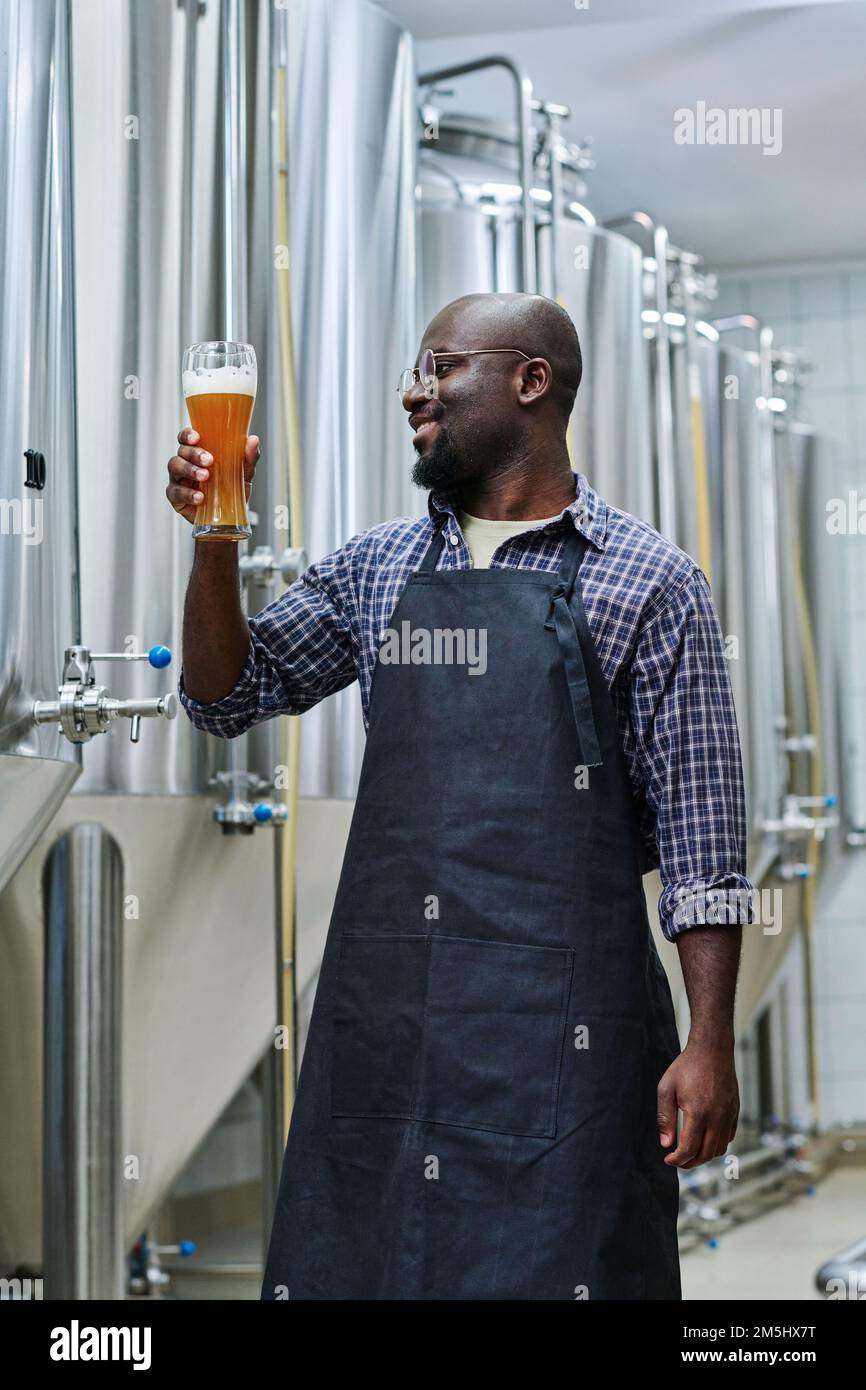 Ingénieur afro-américain tenant un verre de bière en souriant, il se satisfait de la qualité de la boisson Banque D'Images