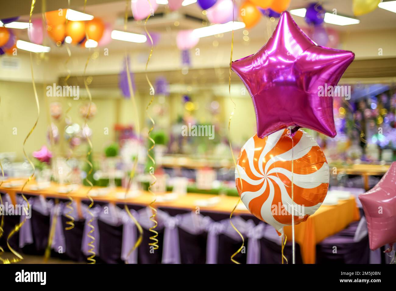 deux ballons remplis d'hélium en forme d'étoile et un lollipop sur le fond d'une salle de fête décorée Banque D'Images