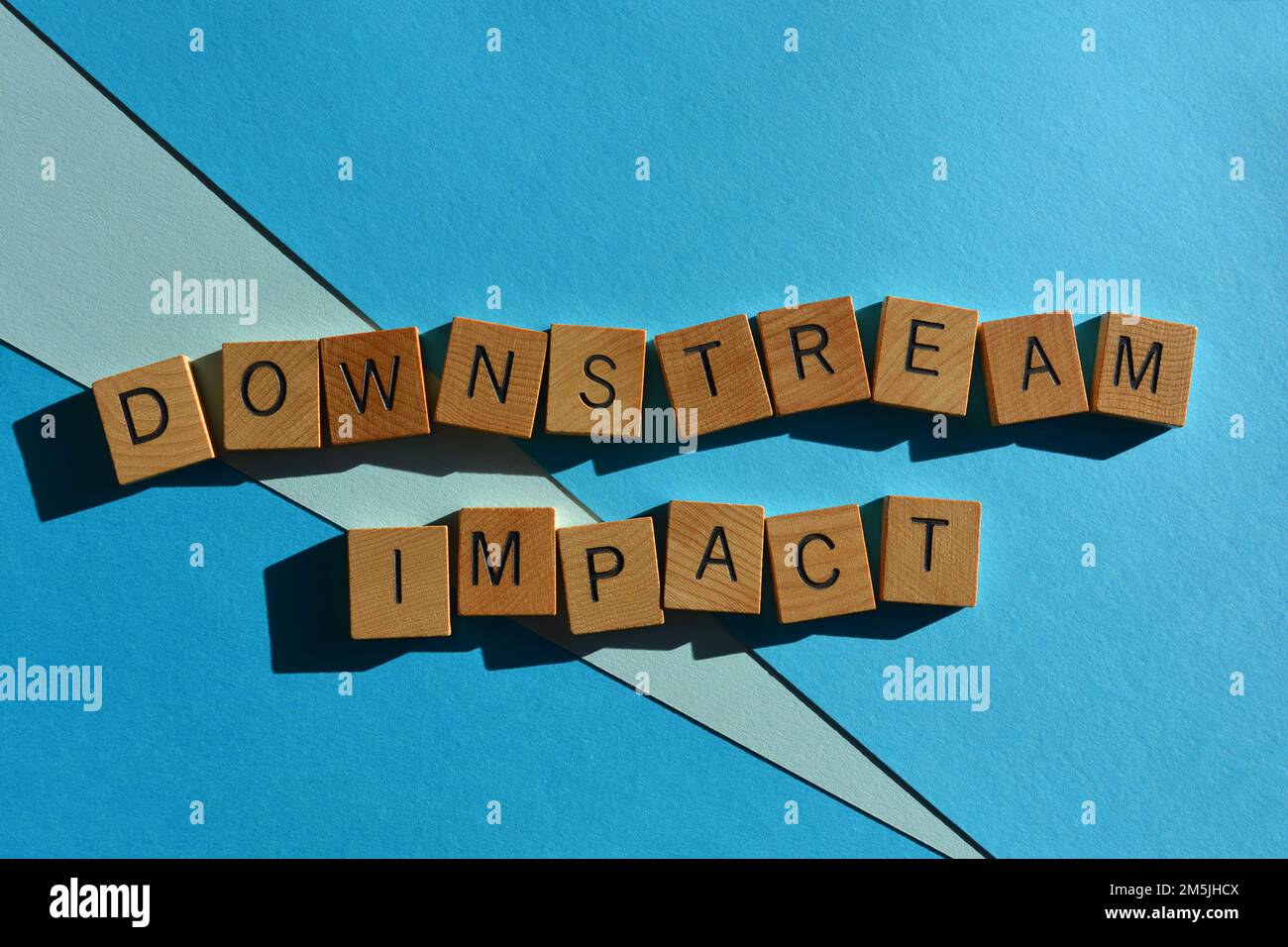 Impact en aval, expression de mot à la mode d'affaires en lettres de l'alphabet en bois isolées sur fond bleu Banque D'Images