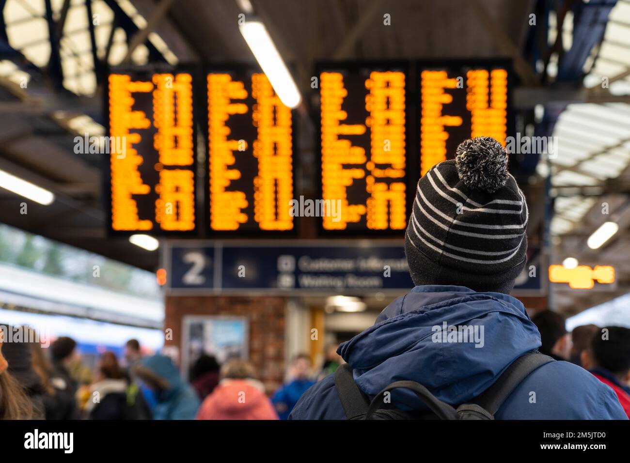 Un homme dans un chapeau de galet à la gare de Basingstoke regardant le panneau de départ du train. Concept: Retards, retards de services, trains annulés Banque D'Images