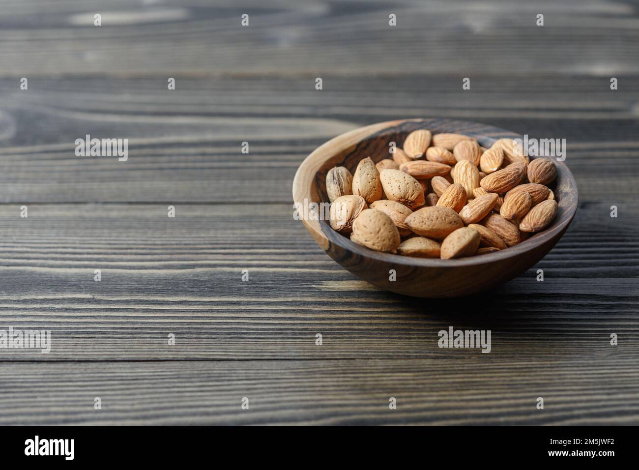Amandes et amandes crues pelées en carapace dans un bol en bois sur fond de bois foncé. Noix, nutrition et concept d'aliments crus Banque D'Images