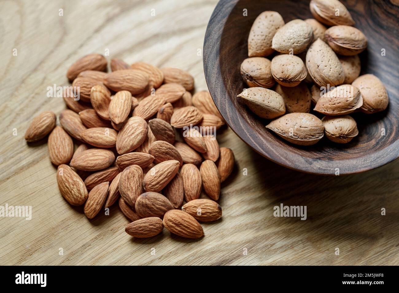 Amandes et amandes crues pelées dans une coquille dans un bol en bois sur fond en bois. Noix, nutrition et concept d'aliments crus Banque D'Images