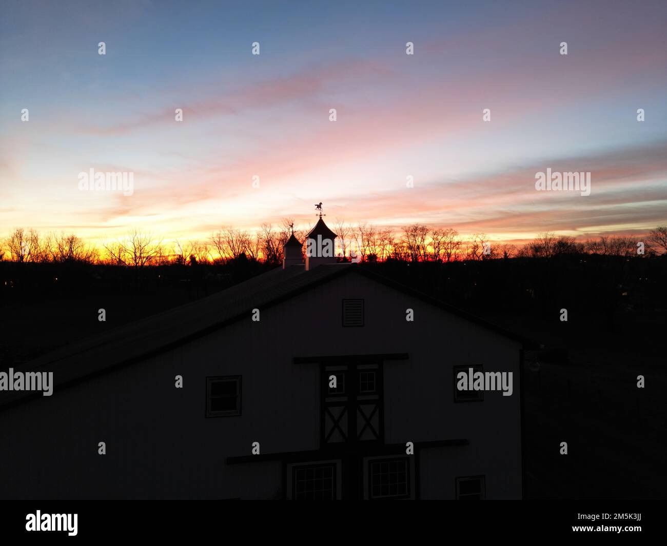 Une maison individuelle et la silhouette de chevaux et de weathervanes contre le ciel orange-rouge au coucher du soleil Banque D'Images