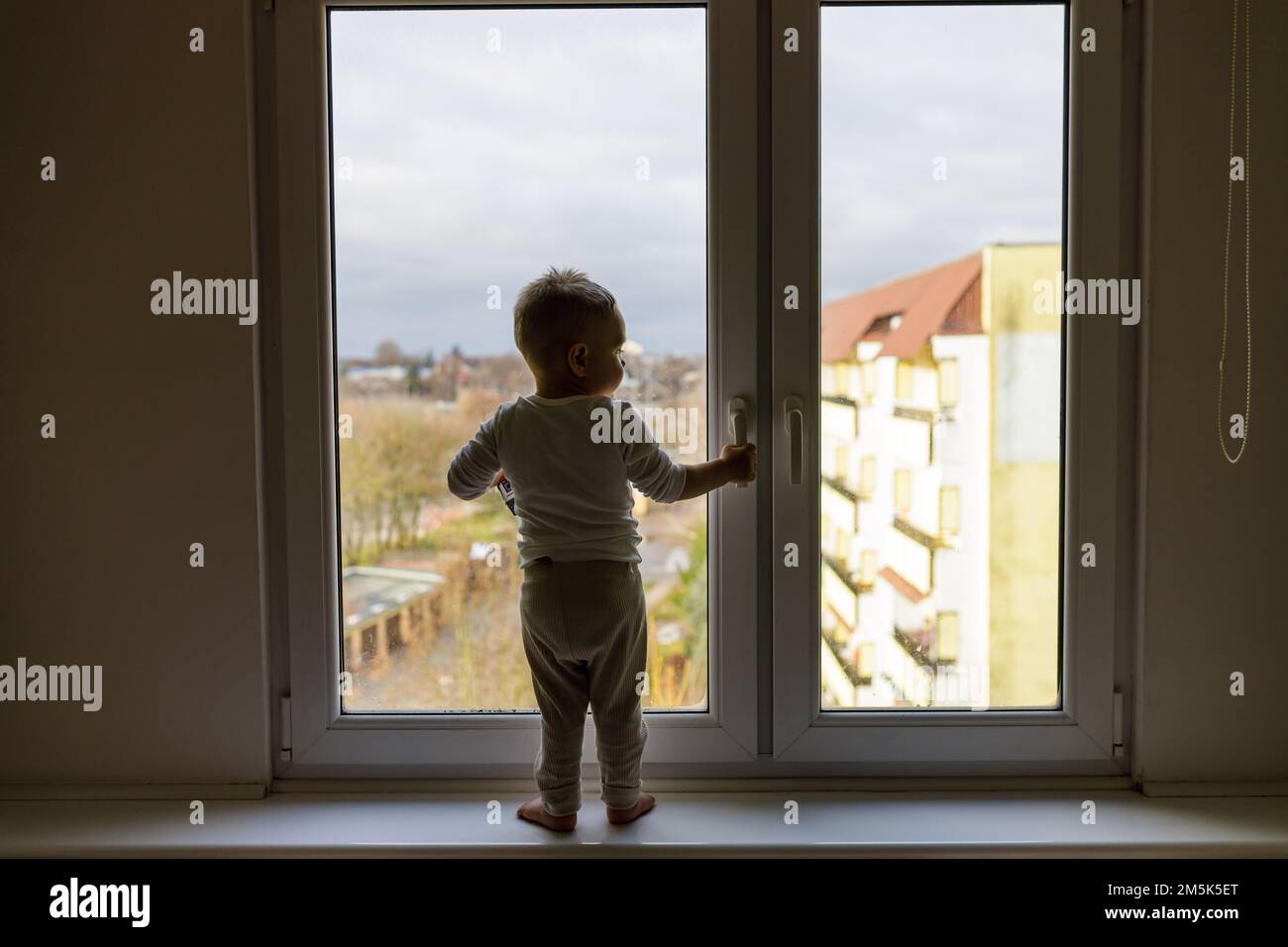 Enfant seul debout sur le rebord de la fenêtre. Situation dangereuse, risque de chute de la vitre. Banque D'Images