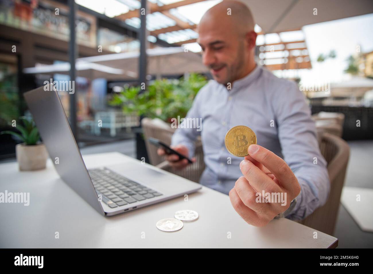 Trader surveille le marché avec son smartphone tout en tenant une pièce de monnaie en bitcoin Banque D'Images