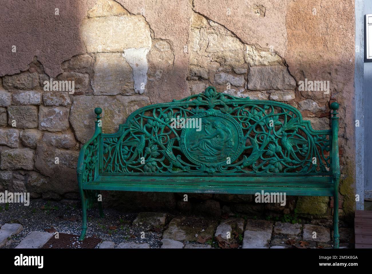 Banc vert en métal élaboré devant un mur en pierre dans une rue, en gros plan Banque D'Images