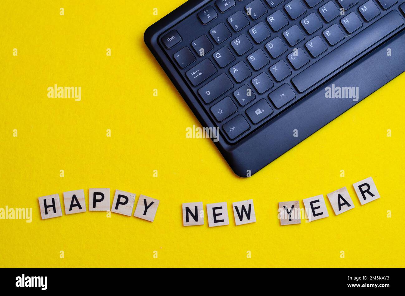 le mot happy new year est imprimé sur des morceaux de bois à côté d'un clavier sur fond jaune. Concept informatique du nouvel an Banque D'Images