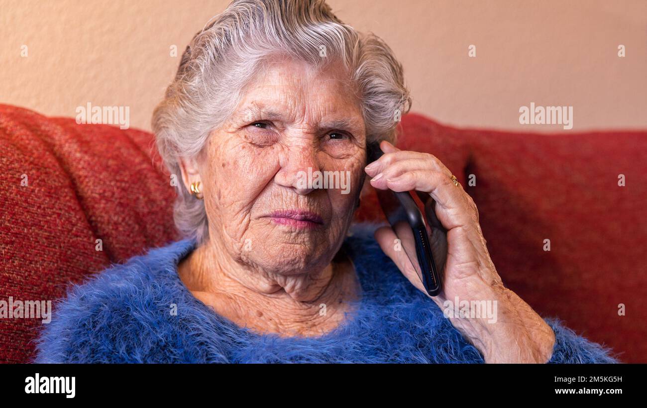 Femme âgée utilisant un smartphone pour parler tout en étant assise sur un canapé à la maison. Grand-mère parlant sur téléphone mobile. Grand-mère de l'ancien âge conver les appels téléphoniques Banque D'Images