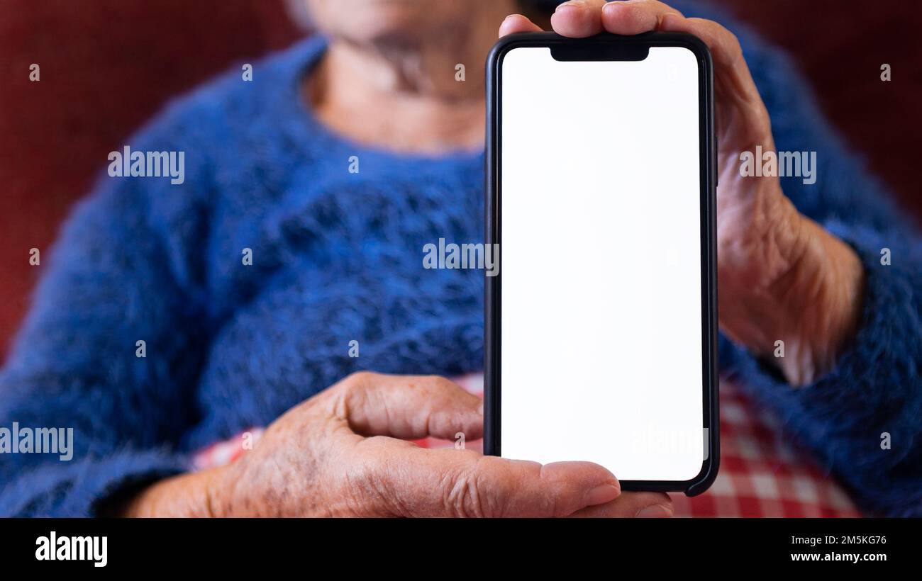Les mains froissées de la vieille femme tient un smartphone avec écran blanc vide pour votre maquette. Gros plan des mains âgées de grand-mère caucasien montrant blanc Banque D'Images