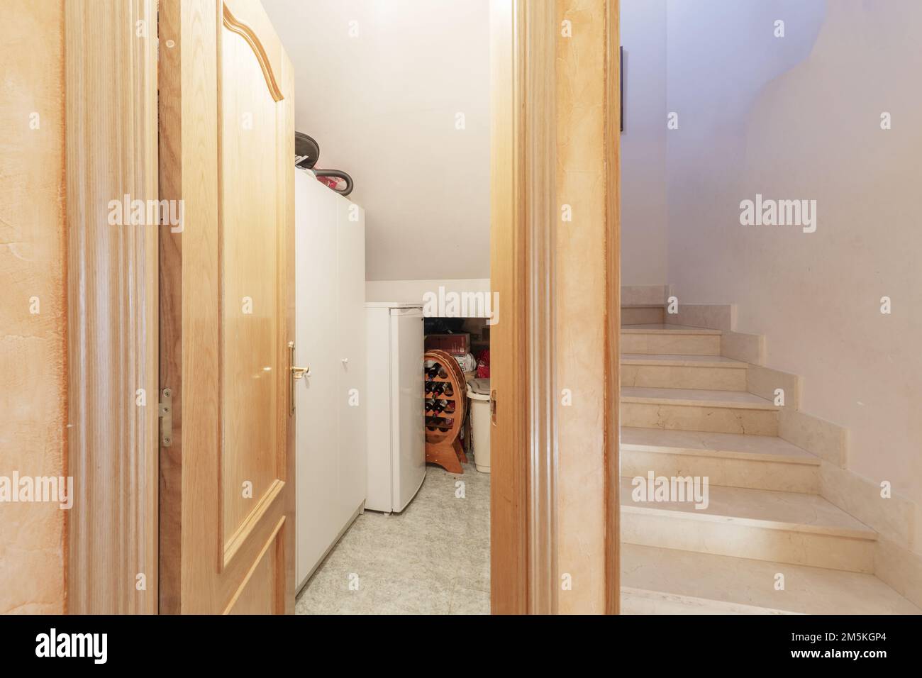 Escaliers d'une maison individuelle avec des marches en marbre couleur crème et un garde-manger avec réfrigérateur et casier à vin Banque D'Images