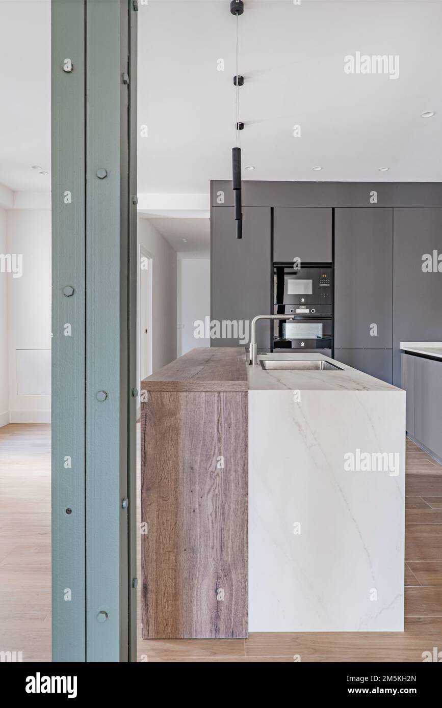 Une cuisine moderne récemment équipée avec une partie de bois, une partie de marbre clair île avec un évier intégré et un pilier en métal peint vert Banque D'Images