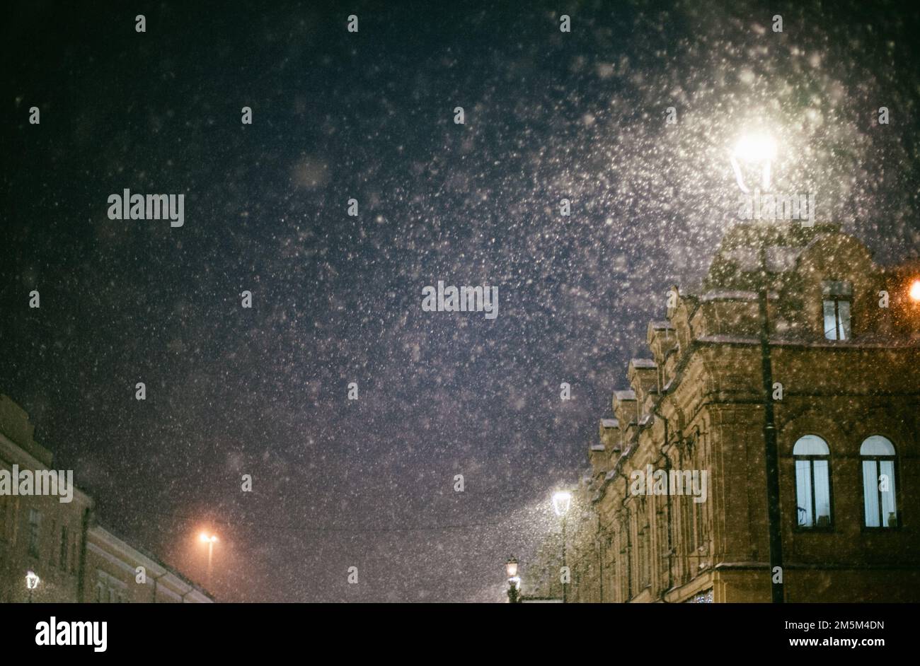 Lanterne lumineuse pendant la chute de neige sur la rue d'hiver de la ville le soir de Noël Banque D'Images