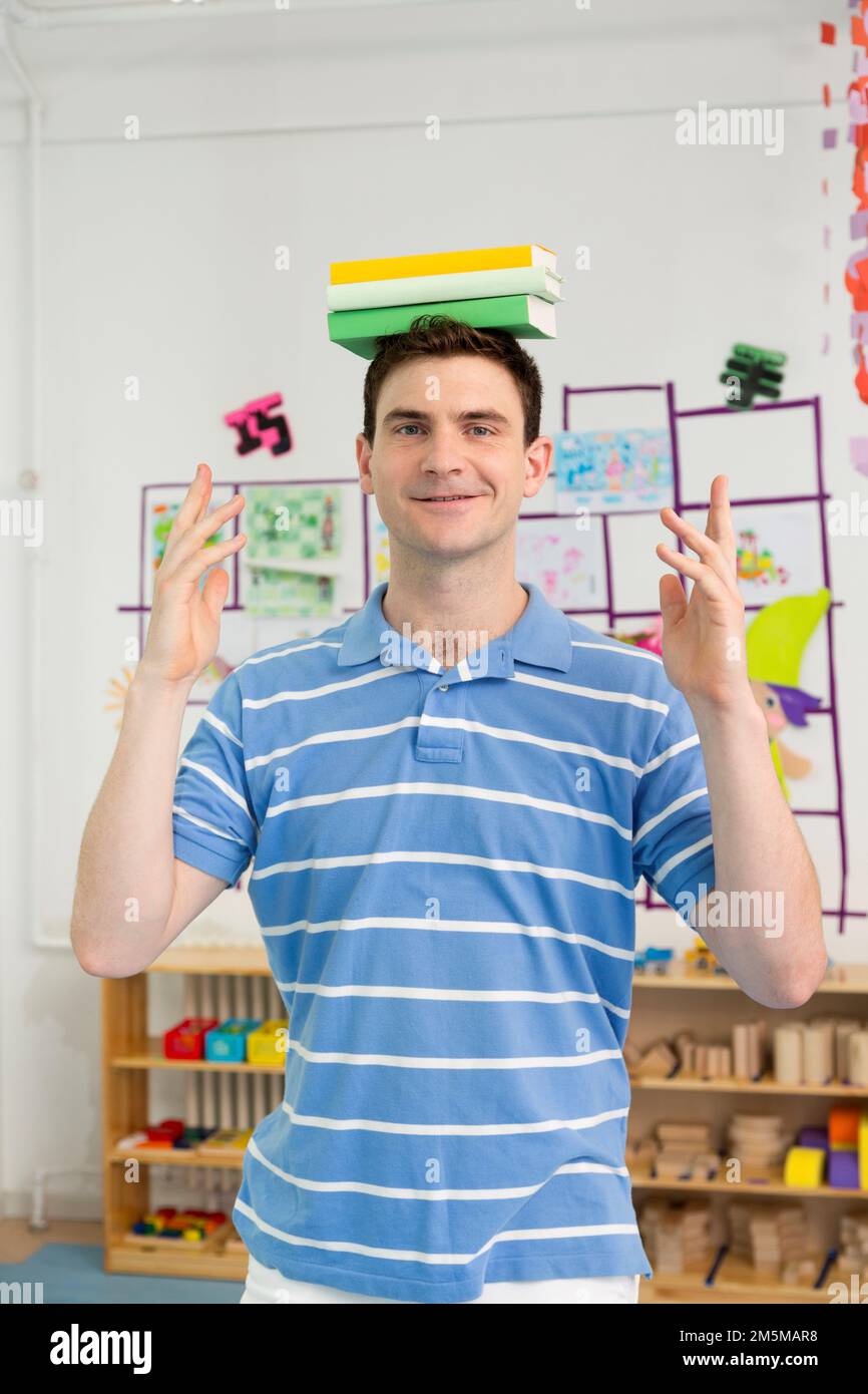 Enseignant de maternelle enseignant de sexe masculin avec un livre sur sa tête Banque D'Images