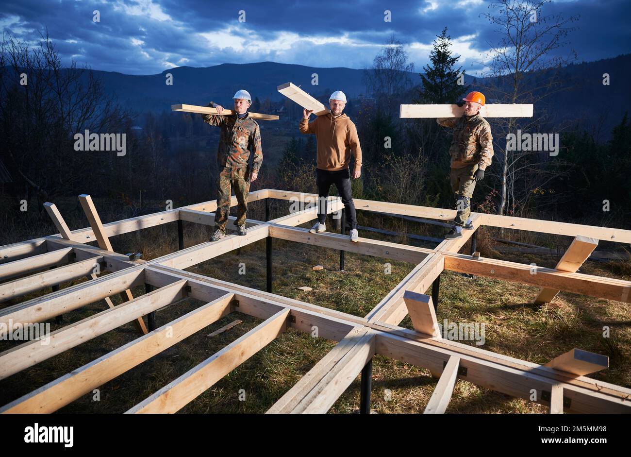 Hommes ouvriers construction de maison de cadre en bois sur la base de pile. Portrait de trois charpentiers transportant des planches en bois pour le charpente de bois. Concept de menuiserie. Banque D'Images