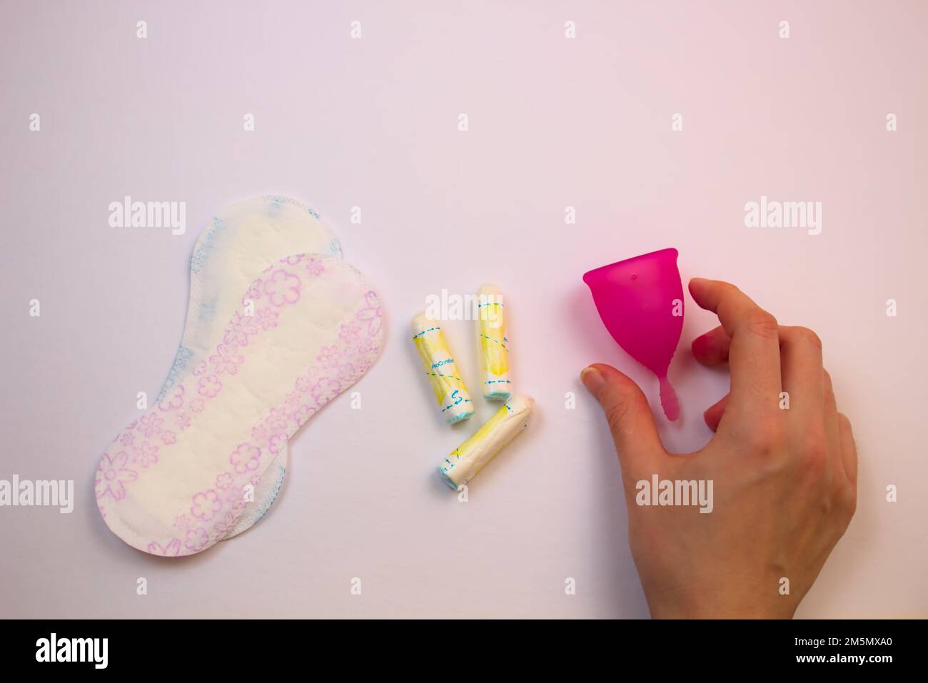 Une vue de haut en bas d'une main sélectionnant une coupe menstruelle rose parmi une variété de produits d'hygiène, en se concentrant sur la transition vers le pe écologique et réutilisable Banque D'Images