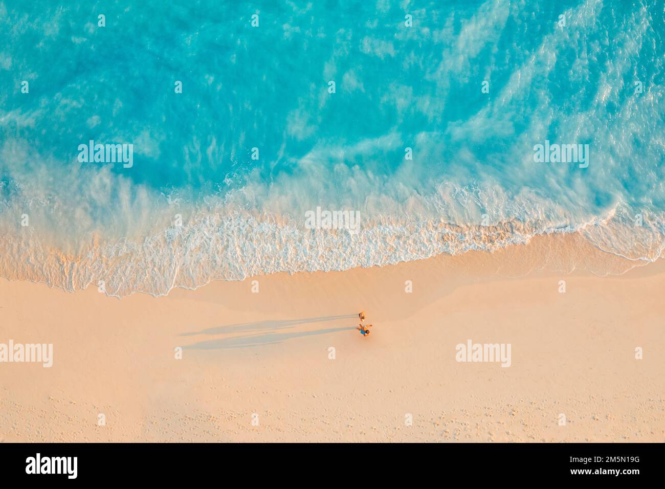 Vue aérienne de la plage incroyable avec couple marchant dans la lumière du coucher du soleil près de la mer turquoise. Vue de dessus de la plage d'été, inspiration romantique Banque D'Images