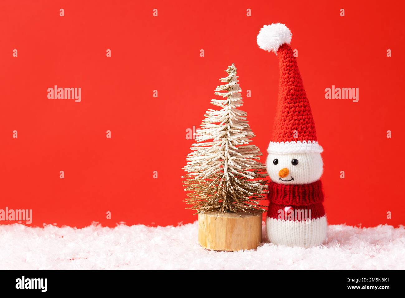 Composition de conte de fées de Noël d'un bonhomme de neige tricoté dans un chapeau et un chandail du Père Noël. Petit arbre de Noël. Banque D'Images