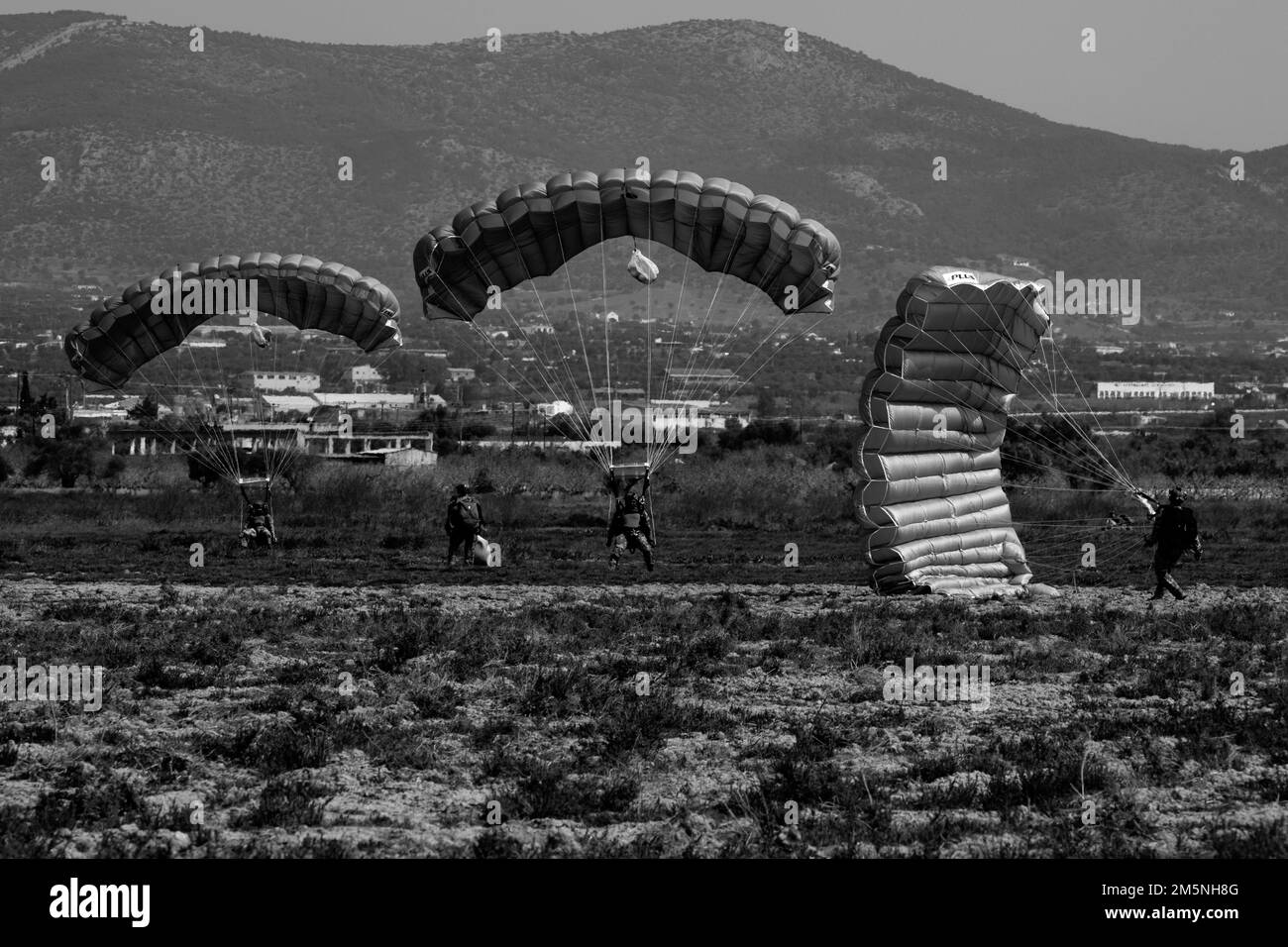 En vue de l'exercice Orion, les membres des forces spéciales d'opérations grecques (SOF) atterrissent dans la zone de chute près d'Elefsina, en Grèce, pendant une opération aérienne pendant qu'un U.S. Le soldat de la SOF observe après avoir rassemblé son parachute, 29 mars 2022. L'exercice Orion renforce la Grèce en tant que chef de file régional des OES, améliore l'interopérabilité dans de multiples domaines et renforce les relations avec les partenaires de l'OTAN et des pays non membres de l'OTAN. L'exercice met l'accent sur les capacités opérationnelles, les collaborations internationales et la formation en matière de guerre conventionnelle et hybride. Banque D'Images