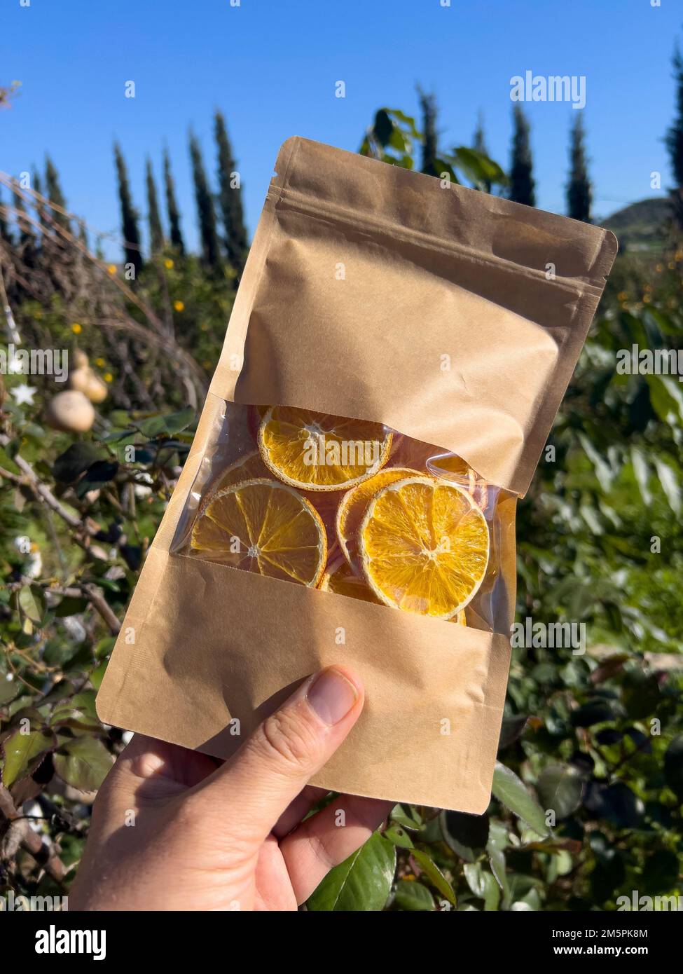 Copeaux d'orange séchés naturels dans un sac de papier recyclé brun avec valve et joint d'étanchéité maintenu par la main humaine sous la lumière du soleil. Arrière-plan nature, espace de copie Banque D'Images Copeaux d'orange séchés naturels dans un sac de papier recyclé brun avec valve et joint d'étanchéité maintenu par la main humaine sous la lumière du soleil. Arrière-plan nature, espace de copie Banque D'Images