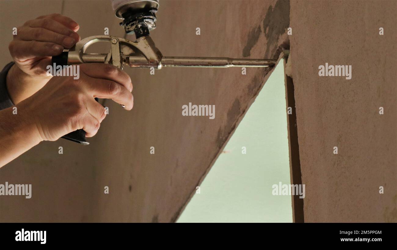 fixation de la pente de la fenêtre dans l'ouverture à l'aide d'un pistolet de montage et de mousse, collage du matériau sur la mousse de polyuréthane tout en travaillant avec un pistolet de construction Banque D'Images