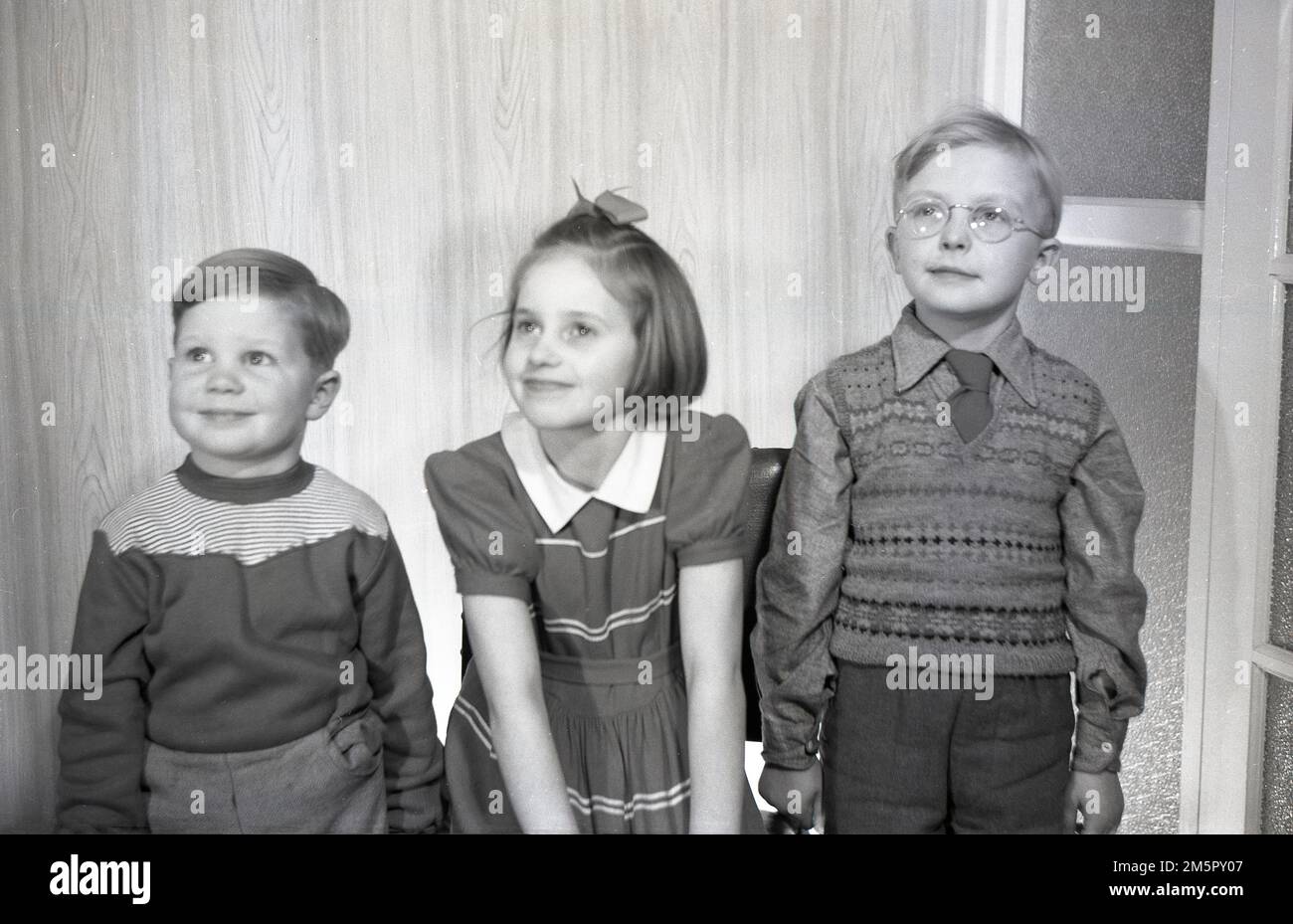 Années 1950, historique, à l'intérieur, trois enfants représentent leur photo dans les vêtements de l'époque, le petit garçon portant un débardeur sans manches et la petite fille avec un noeud de cheveux, Angleterre, Royaume-Uni. Banque D'Images