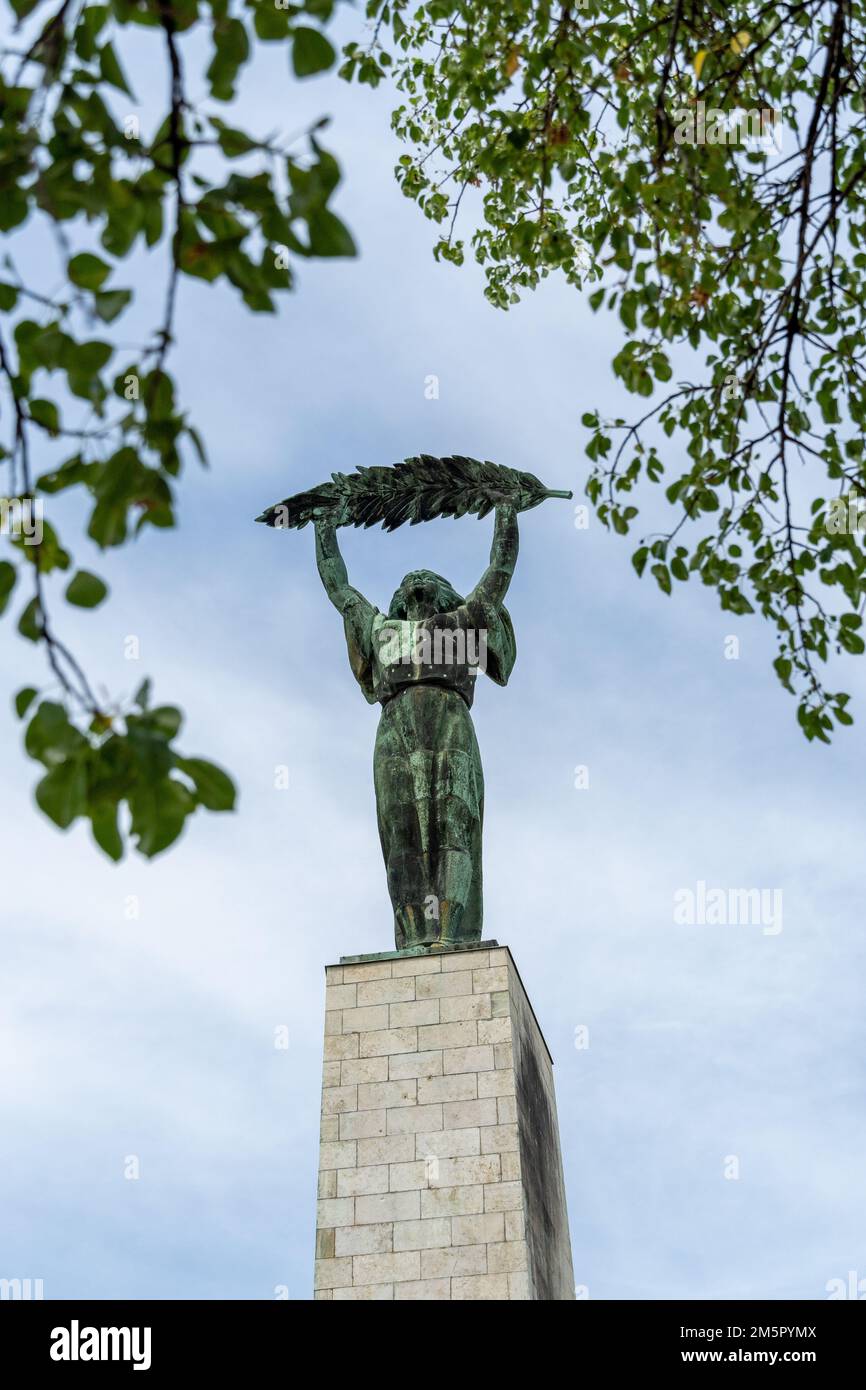 La statue historique de la liberté sur la colline de Gellert devant un ciel nuageux et des feuilles vertes à Budapest, Hongrie Banque D'Images