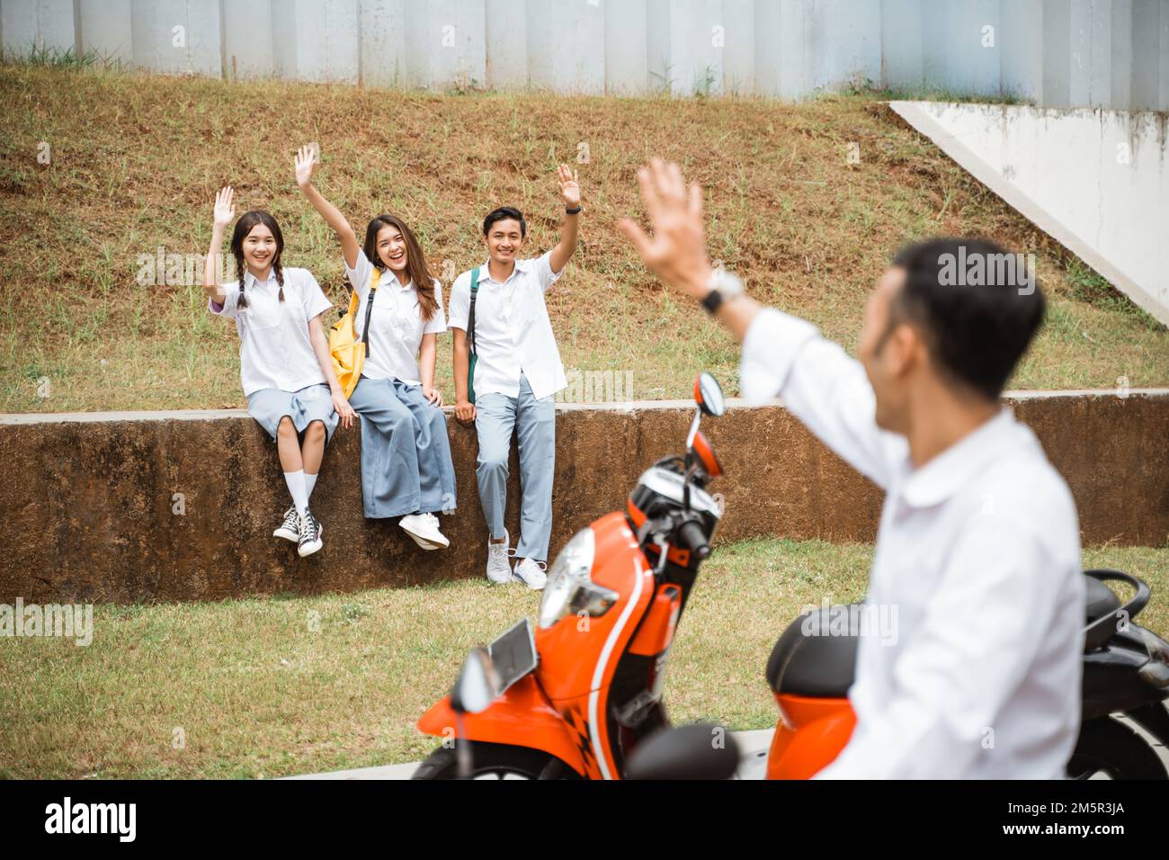 Trois enfants du secondaire rencontrent un ami qui est venu en moto Banque D'Images