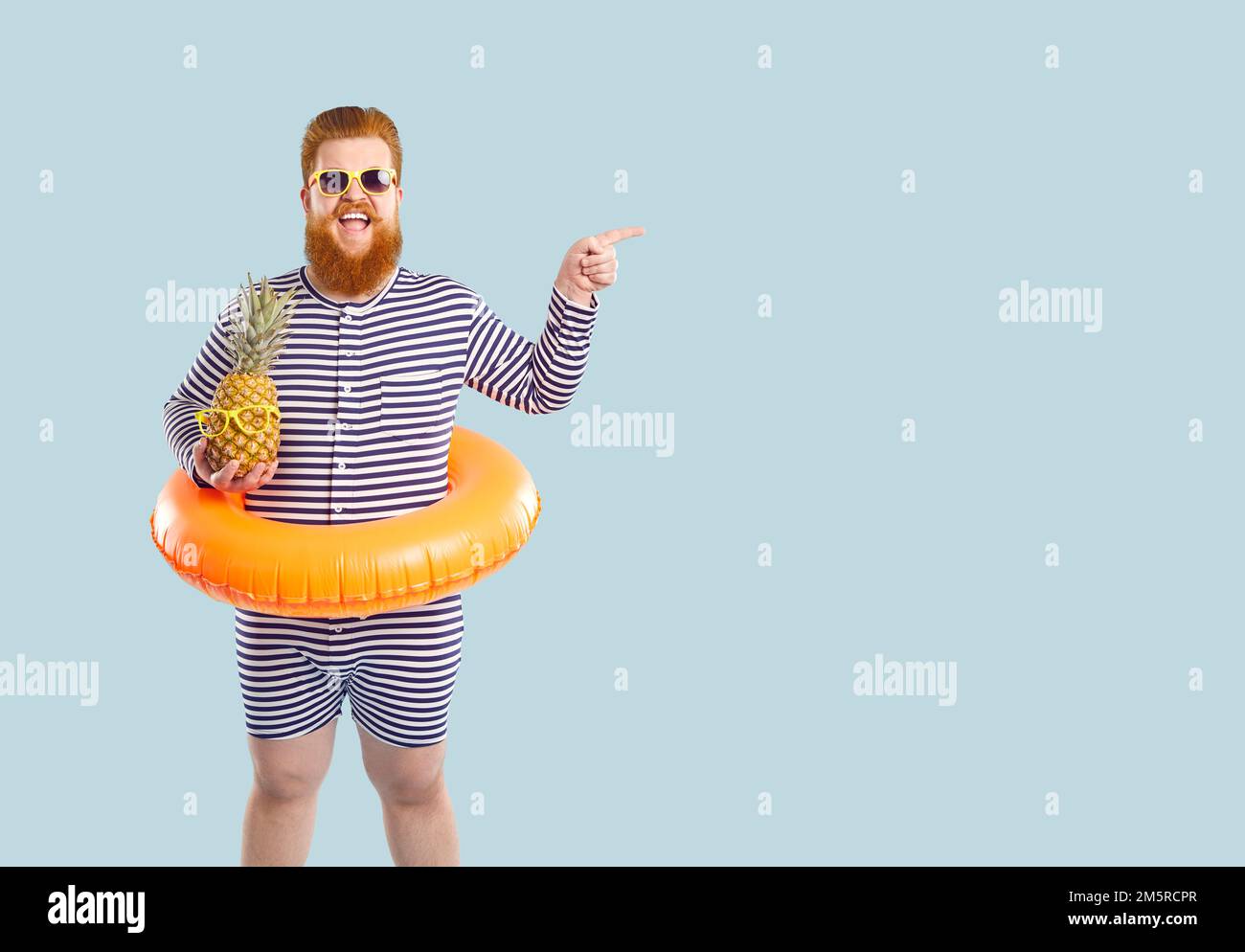 Jeune redhead heureux homme caucasien touriste avec la bouée à vie sur la ceinture tenant des supports d'ananas en studio Banque D'Images