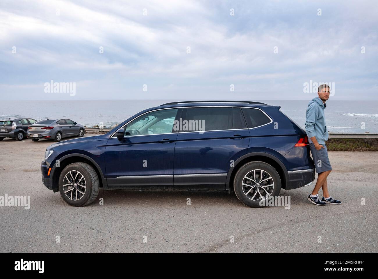 Homme se penchait sur une voiture bleue avec un paysage marin et un ciel nuageux en arrière-plan Banque D'Images