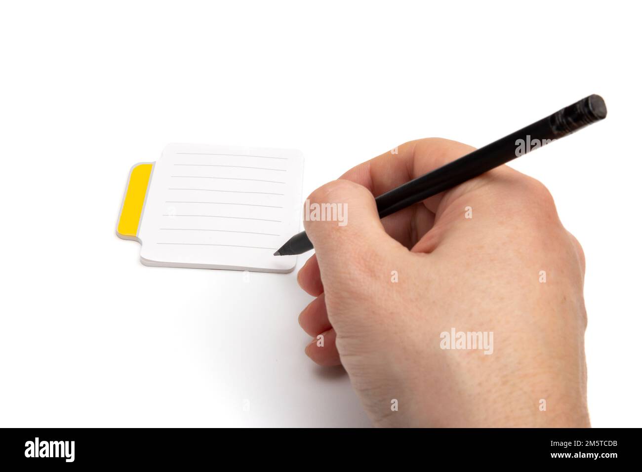 Main avec crayon écrivant sur des notes autocollantes vierges à petites lignes avec une languette jaune sur le côté gauche de la feuille de papier, isolée sur fond blanc, vue rapprochée Banque D'Images Main avec crayon écrivant sur des notes autocollantes vierges à petites lignes avec une languette jaune sur le côté gauche de la feuille de papier, isolée sur fond blanc, vue rapprochée Banque D'Images