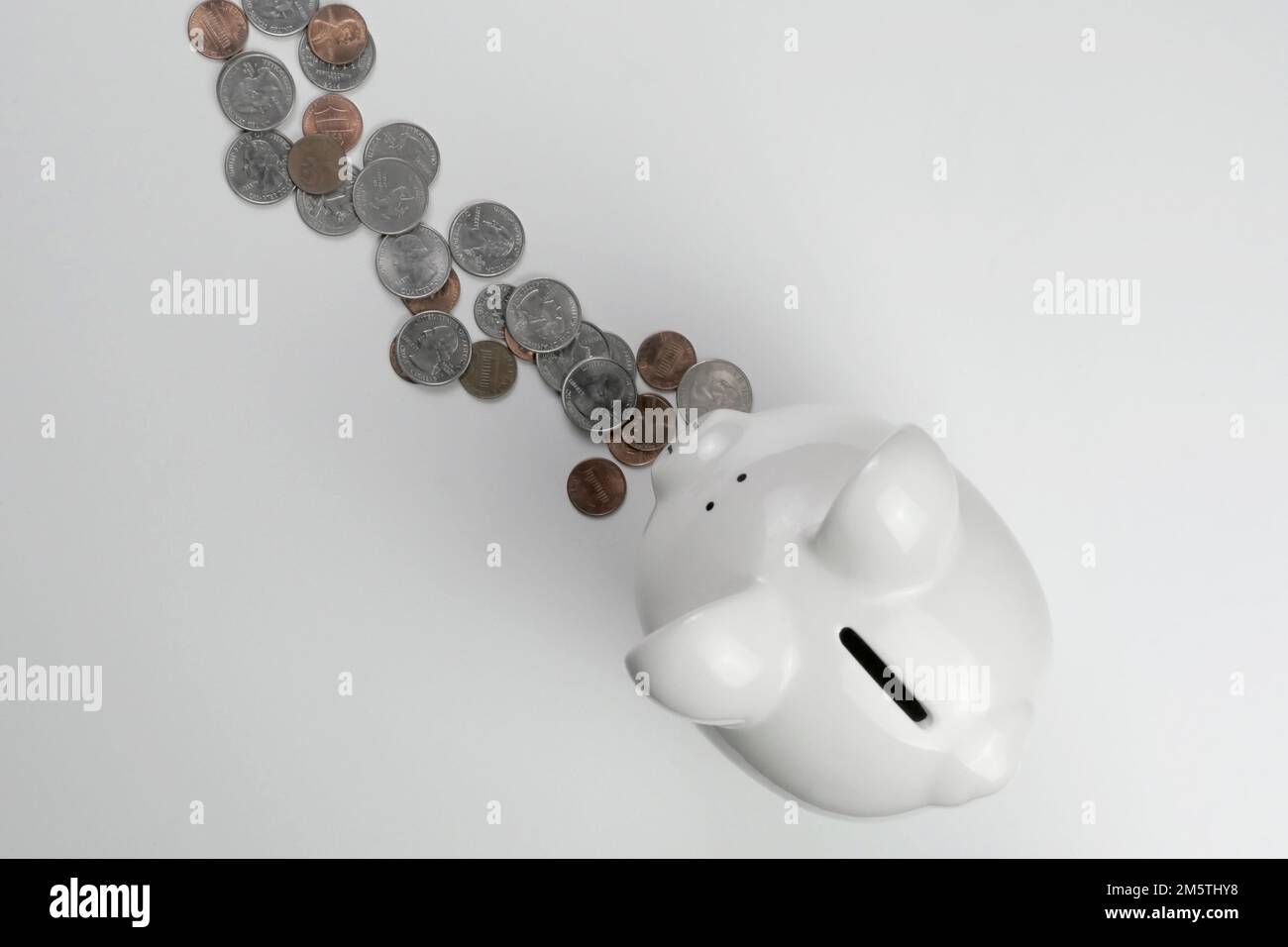 Jolie tirelire en céramique blanche sur fond blanc avec des pièces en monnaie américaine : pièces de monnaie, pièces de cinq cents, pièces de dix cents, pièces de dix cents et pièces de monnaie Banque D'Images