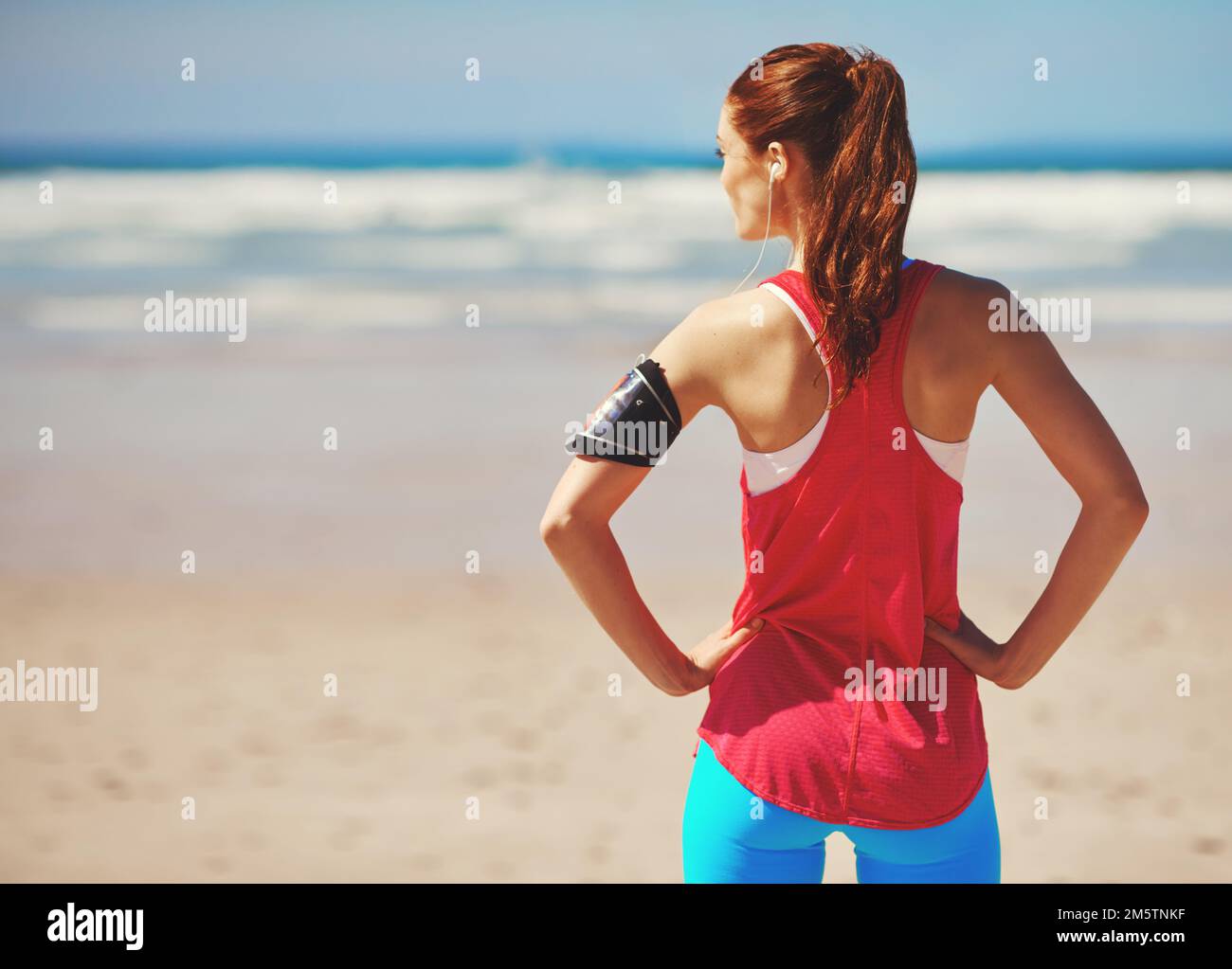 Faites de l'exercice avec une vue magnifique. Vue arrière d'une jeune femme debout avec ses mains sur les hanches, sur la plage. Banque D'Images