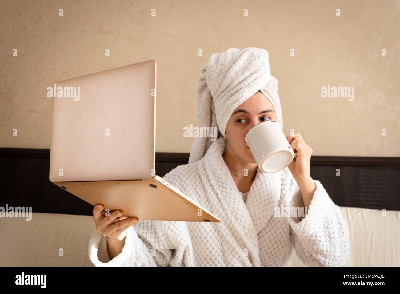 Femme travaillant à la maison dans une robe de chambre blanche en éponge avec une serviette au-dessus de sa tête Banque D'Images
