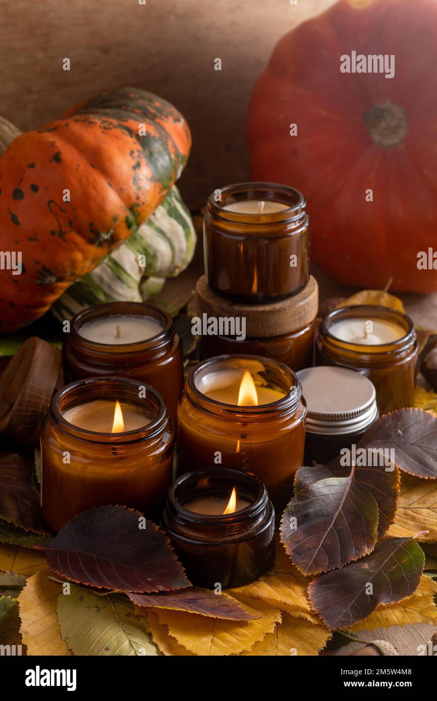 Les bougies de soja brûlent dans des pots en verre. Feuilles d'arbre, citrouille. Confort à la maison. Bougie dans un pot brun. Parfum et lumière. Bougie parfumée faite à la main. Aromathérapie. Ambiance d'automne. Décoration chaleureuse à l'automne. Banque D'Images