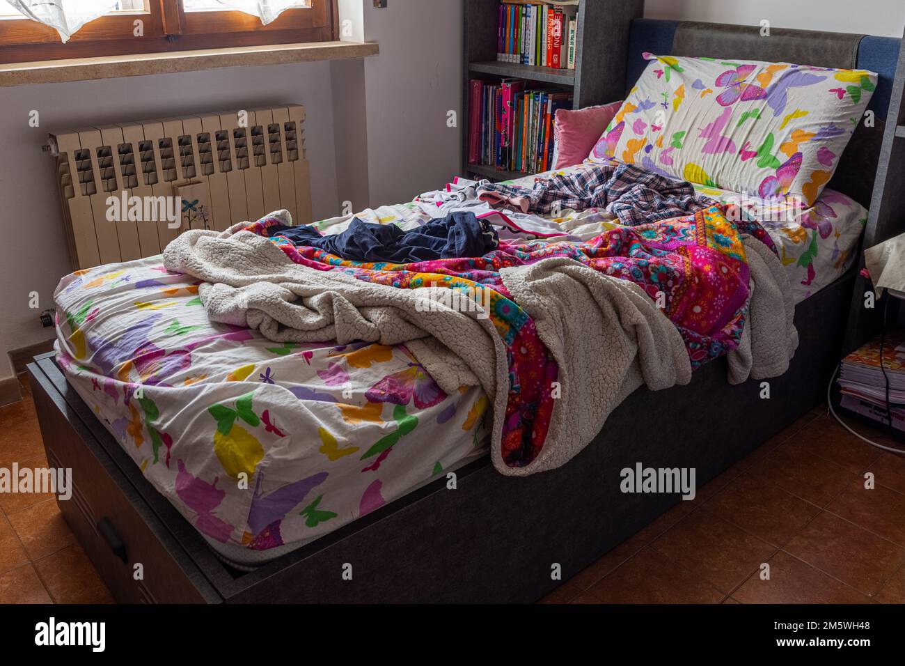 Lit désordonné non fait dans une chambre. Couverture colorée, oreillers, draps froissés. Style de vie, maison, routine matinale. Banque D'Images