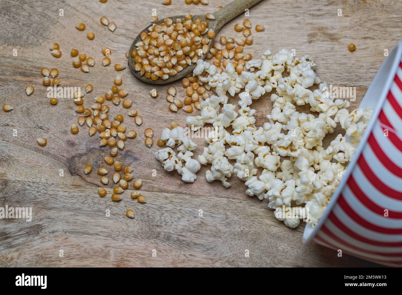 Pop-corn (éclaté) et noyaux dispersés sur une surface en bois rustique avec une cuillère. Ingrédients d'aliments à grignoter. Banque D'Images