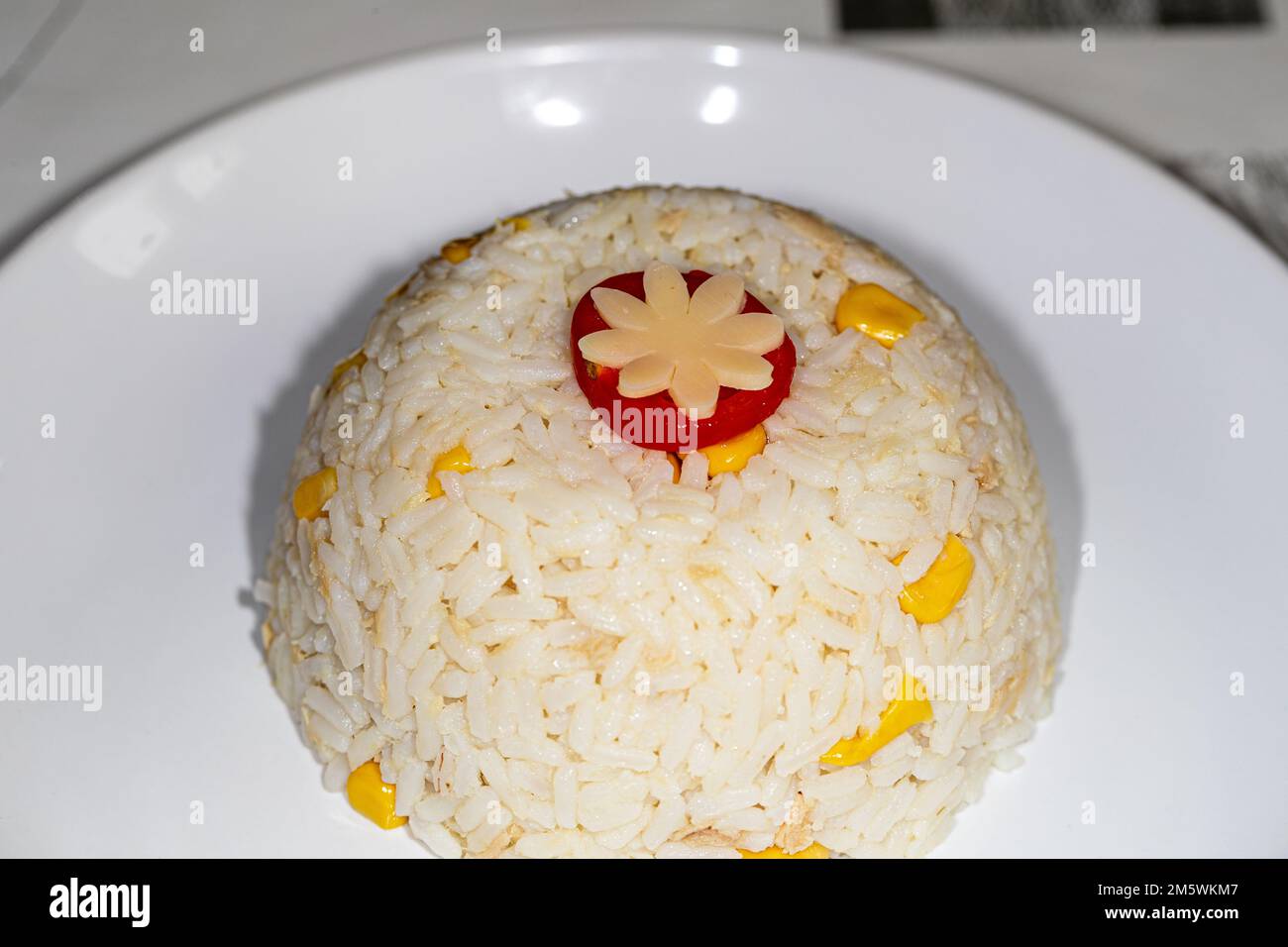 Portion de riz blanc servie sur une assiette, garnie de fleurs de légumes sculptées et de maïs. Repas simple. Banque D'Images