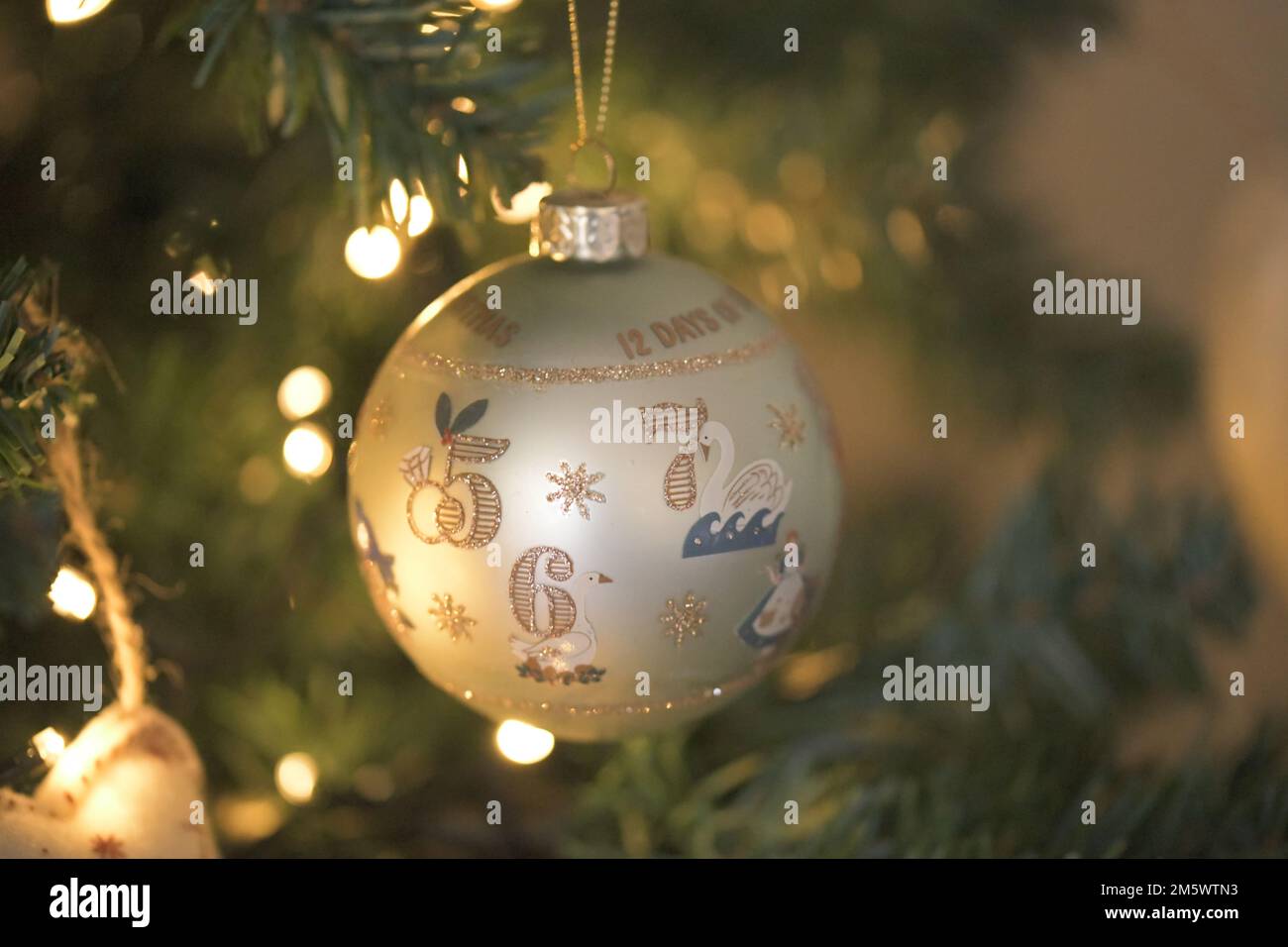 Une boule de crème et d'or avec les numéros cinq, six, sept accrochés à un arbre de Noël lumineux et chaud Banque D'Images