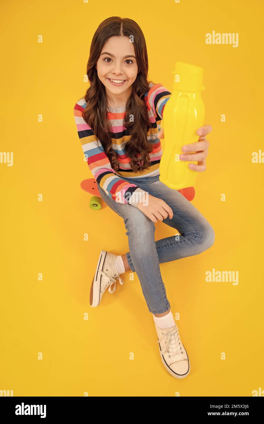 Une adolescente tient une bouteille d'eau isolée sur fond jaune. Bouteille d'eau et vie saine. Santé et équilibre de l'eau. Concept boissons et boissons Banque D'Images