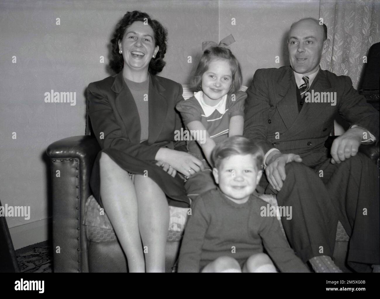 Années 1950, historique, photo de famille, une mère, un père et leurs deux jeunes enfants assis ensemble sur un petit canapé, grands sourires pour leur photo, Angleterre, Royaume-Uni. Banque D'Images