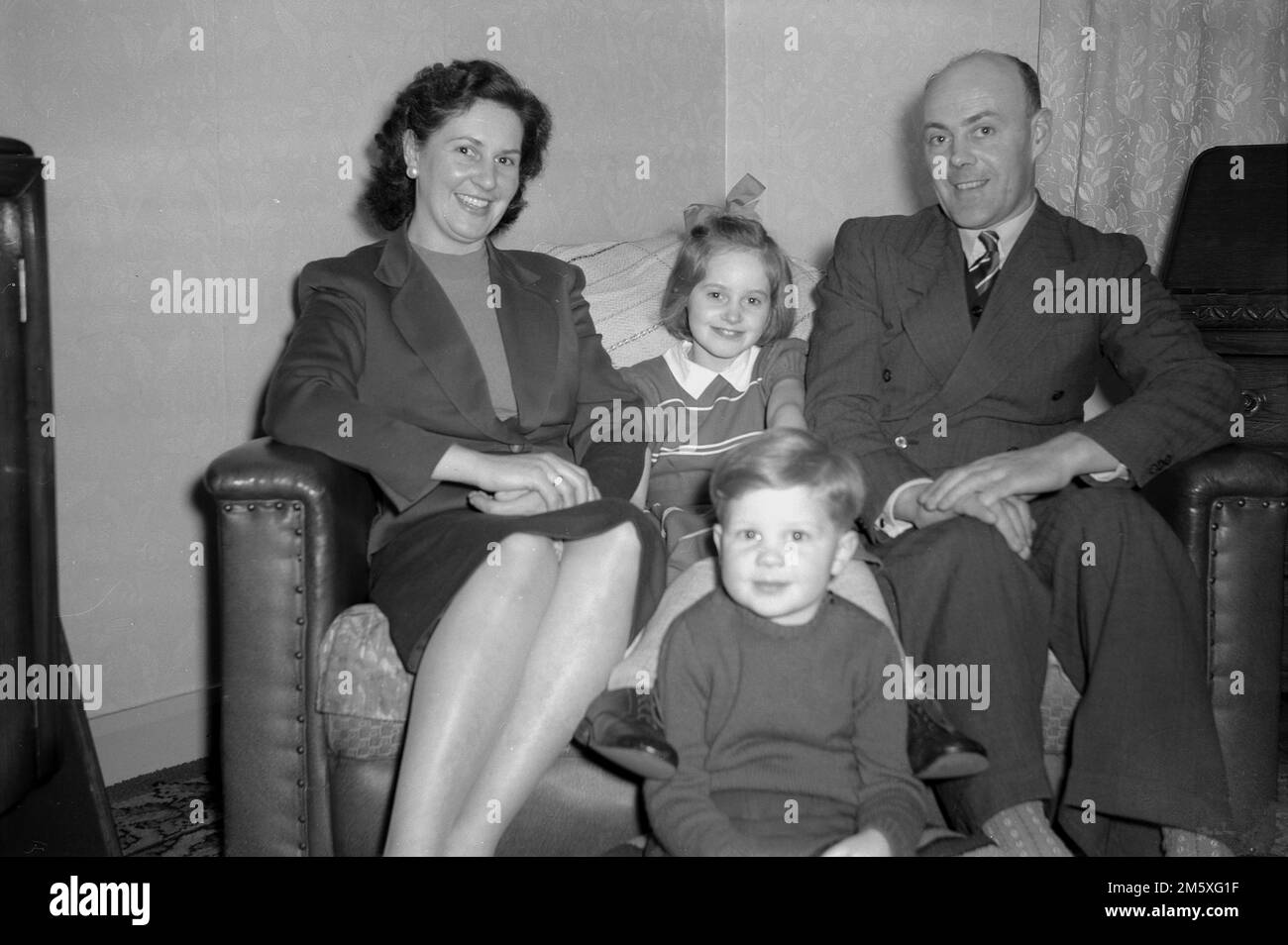 Années 1950, historique, photo de famille, une mère, un père et leurs deux jeunes enfants assis ensemble sur un petit canapé, souriant pour leur photo, Angleterre, Royaume-Uni. Banque D'Images