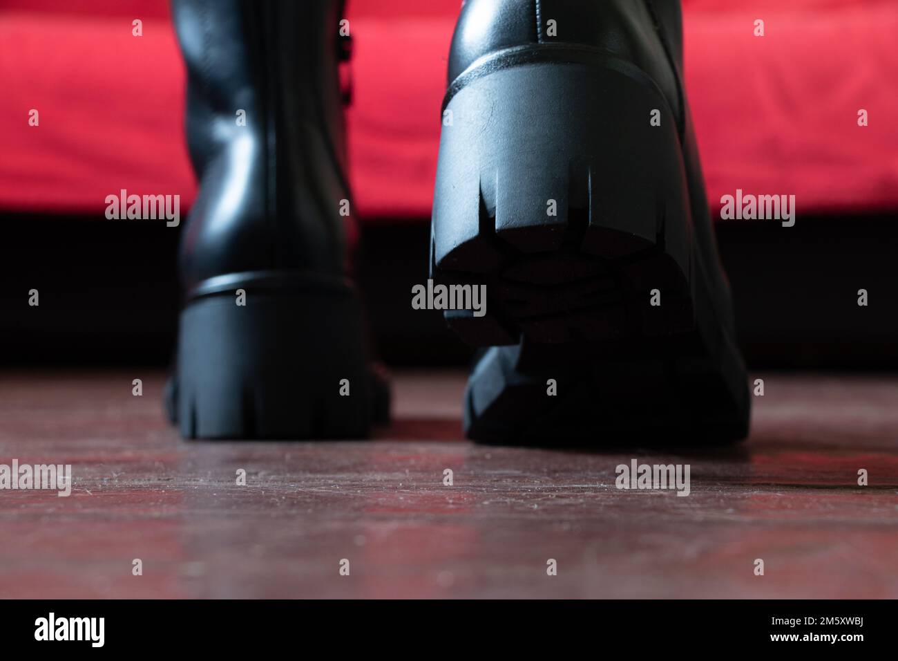 fille en bottes noires hautes sur le vieux sol sale à la maison, chaussures pour femmes, pieds dans les chaussures sur le sol, chaussures sur le plancher en bois Banque D'Images