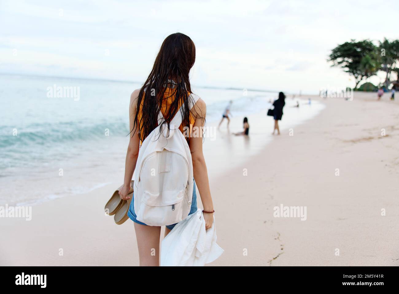 Une jeune femme après avoir nagé dans l'océan avec un sac à dos en vêtements mouillés marche le long de la plage, vacances d'été sur une île près de l'océan à Bali Banque D'Images