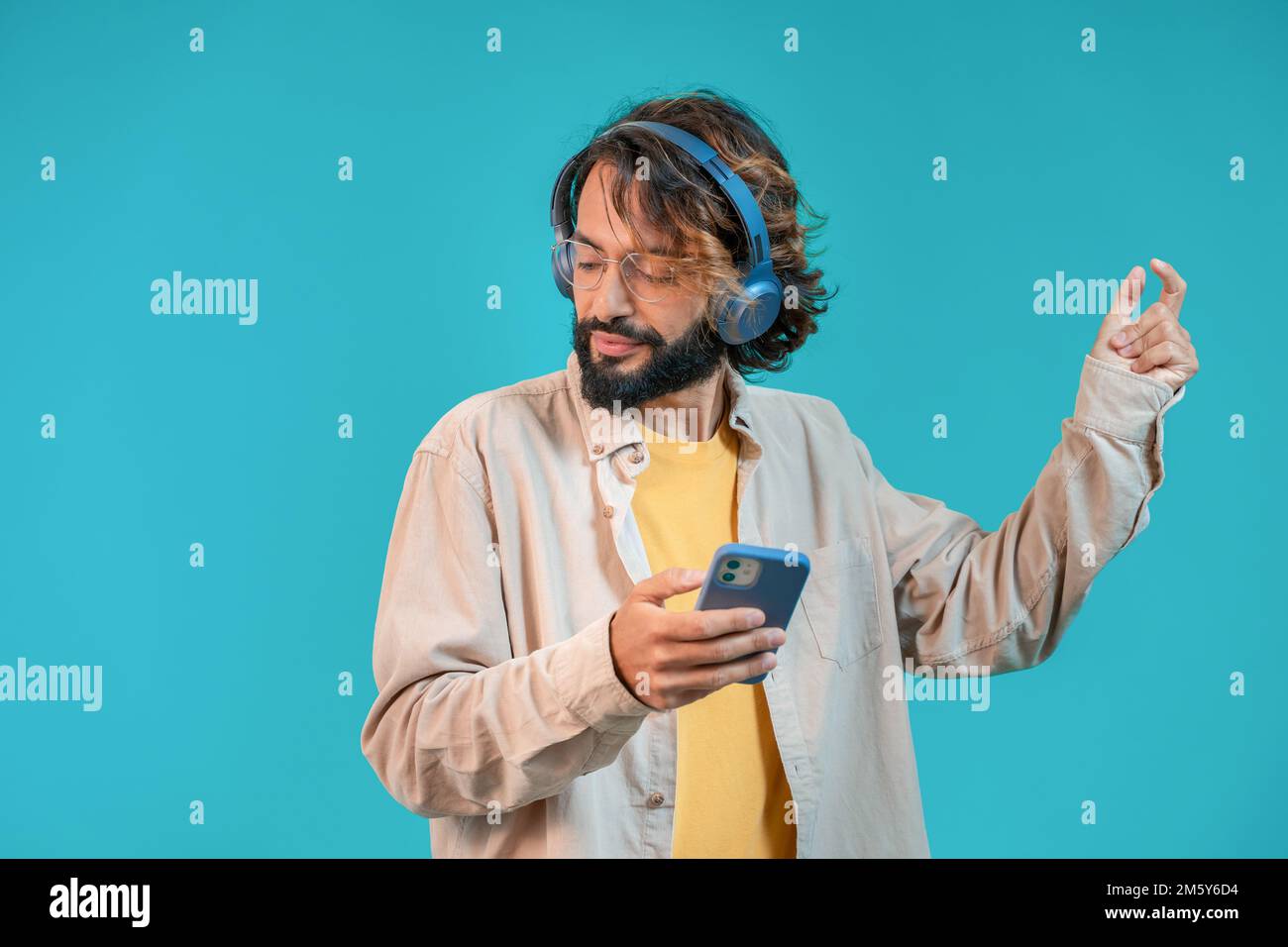 Joyeux homme séduisant dansant sur fond bleu avec un casque et tenant un smartphone Banque D'Images