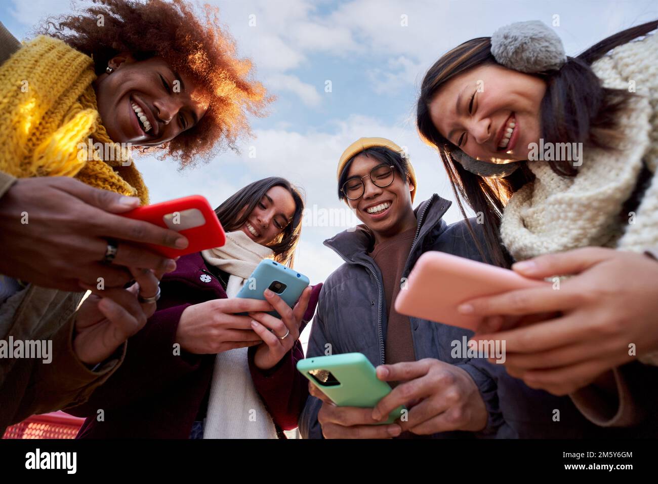 Vue en contre-plongée d'un groupe de jeunes souriants utilisant un téléphone portable. Connexion à la technologie accro Banque D'Images