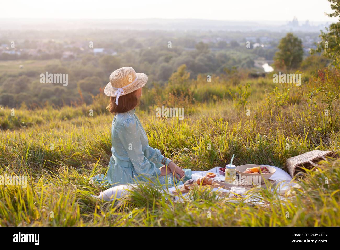 Une femme en robe bleue est assise sur un pique-nique dans un parc avec vue panoramique Banque D'Images