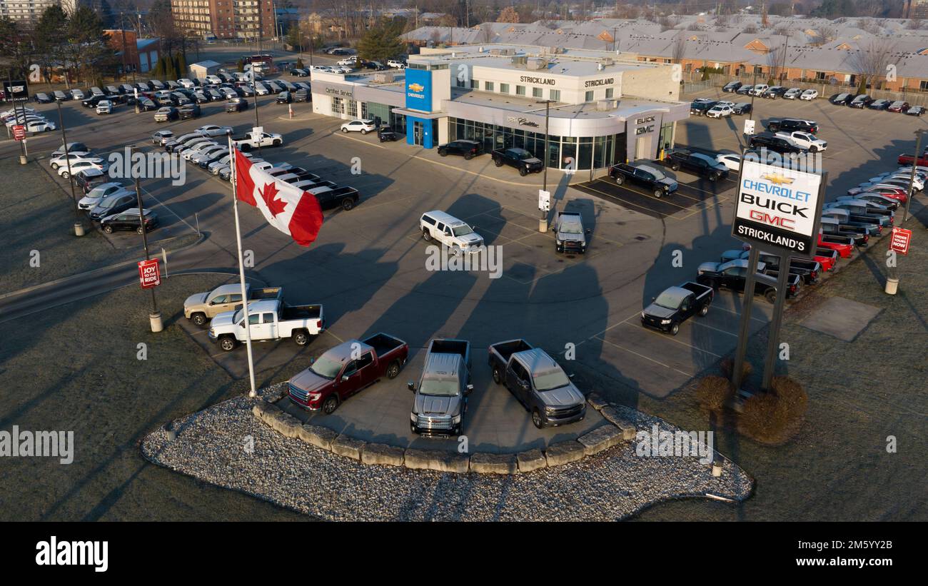 Une photo aérienne devant un concessionnaire Cheverolet, de nouvelles voitures sont vues remplir le stationnement et le drapeau canadien agitant le matin. Banque D'Images