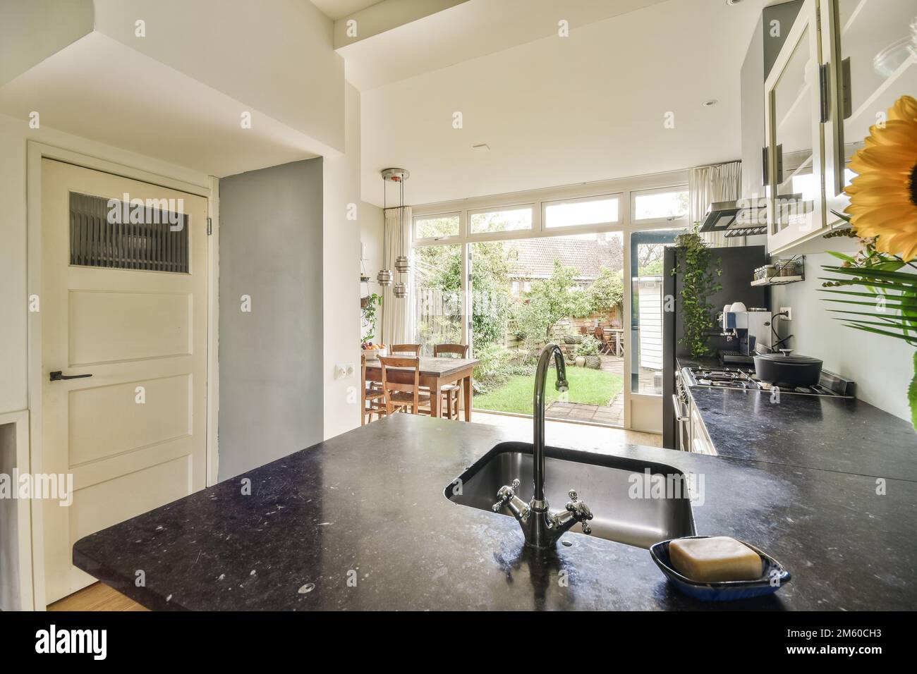 une cuisine et salle à manger dans une maison avec une porte ouverte menant à la terrasse extérieure, il y a un comptoir en granit noir Banque D'Images