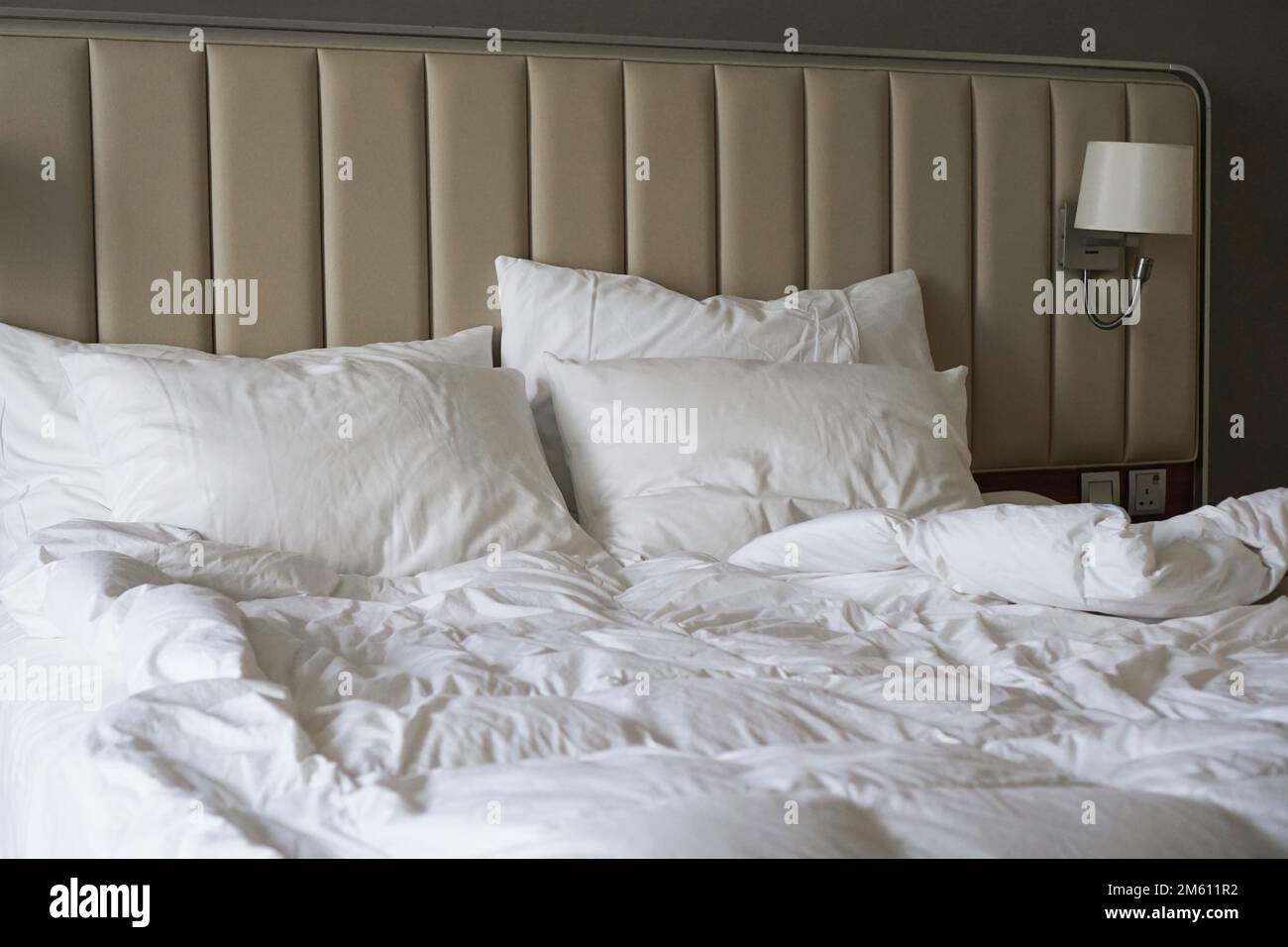 Lit froissé dans une chambre d'hôtel ou à la maison. Draps blancs. Tête de lit rembourrée beige. Vue latérale Banque D'Images